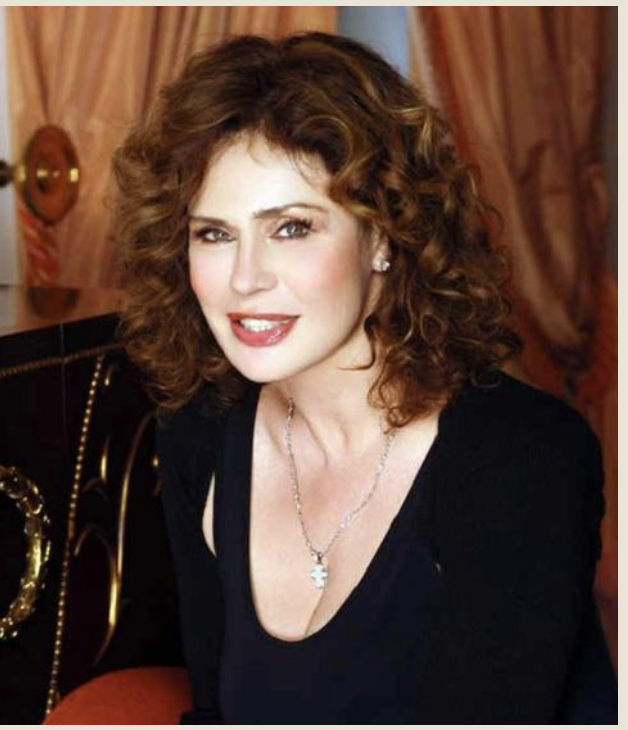 Ritratto ravvicinato di Corinne Cléry sorridente, capelli ricci e abito nero